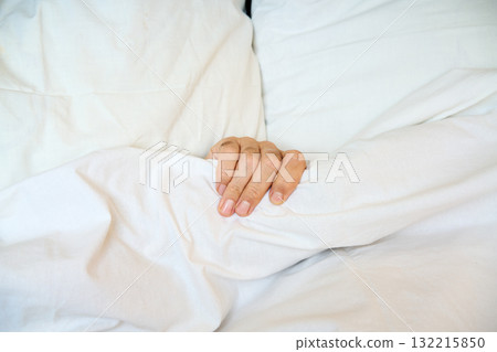Close-up of human hand gripping a white blanket on soft bed 132215850