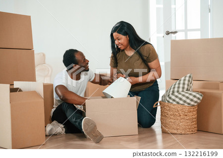 Excited people sitting by the boxes. African American couple are moving into new house Excited people sitting by the boxes. African American couple are moving into new house 132216199