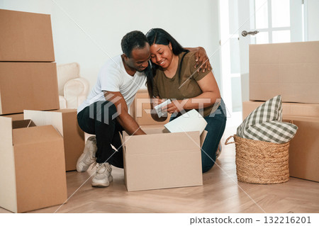 Excited people sitting by the boxes. African American couple are moving into new house 132216201
