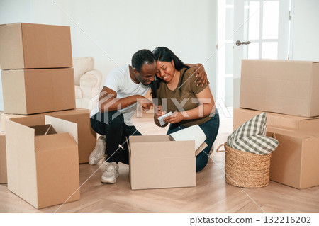 Excited people sitting by the boxes. African American couple are moving into new house 132216202