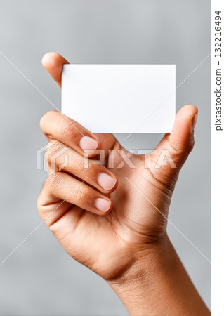 Hand holding blank business card against a soft gray background, showcasing copy space for branding and design purposes in a professional setting 132216494