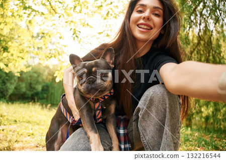 Hand holding camera, doing selfie. Young pretty woman is with her dog in the park 132216544
