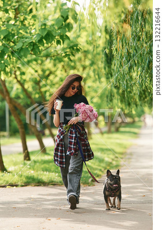 Pink flowers in hands. Young pretty woman is with her dog in the park Pink flowers in hands. Young pretty woman is with her dog in the park 132216644