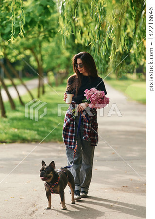 Pink flowers in hands. Young pretty woman is with her dog in the park Pink flowers in hands. Young pretty woman is with her dog in the park 132216646