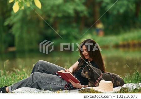 With book, lying down. Young pretty woman is with her dog in the park With book, lying down. Young pretty woman is with her dog in the park 132216673