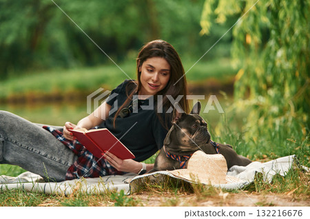 Lying down with book. Young pretty woman is with her dog in the park 132216676