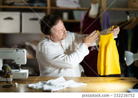 Middle-aged male dressmaker reviewing finished child dress 132216752