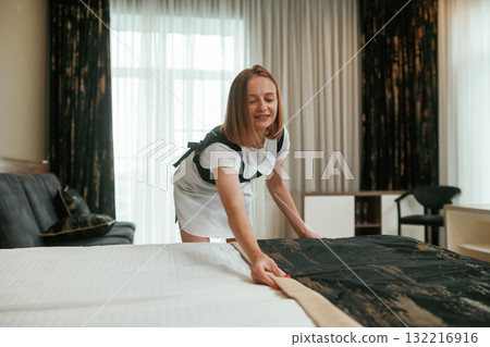 Taking care of bed. Young chambermaid is in hotel room 132216916