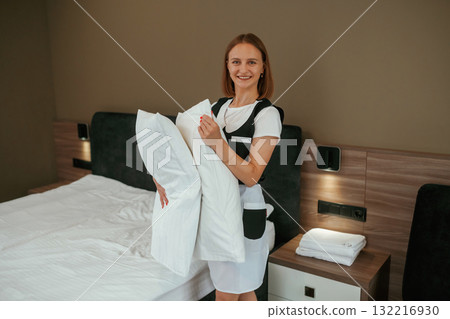 Pillows in hands. Young chambermaid is in hotel room Pillows in hands. Young chambermaid is in hotel room 132216930
