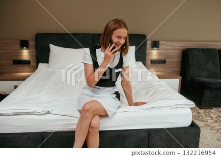 Talking by phone. Young chambermaid is in hotel room Talking by phone. Young chambermaid is in hotel room 132216954