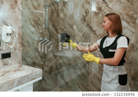 In yellow gloves, cleaning. Young chambermaid is in hotel room In yellow gloves, cleaning. Young chambermaid is in hotel room 132216956