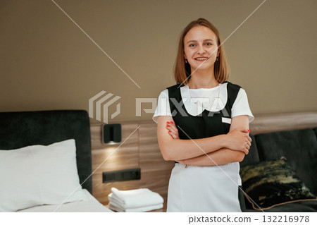With arms crossed, standing. Young chambermaid is in hotel room With arms crossed, standing. Young chambermaid is in hotel room 132216978