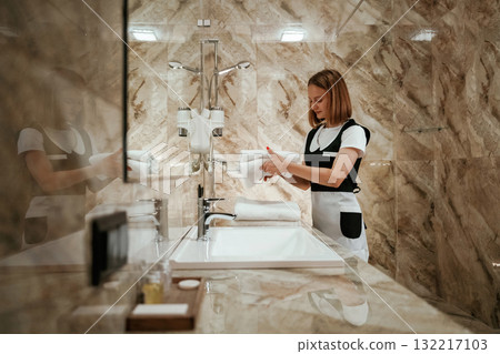 Bathroom cleaning. Young chambermaid is in hotel room 132217103