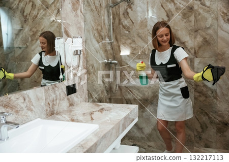 Green washing product, cleaning the glass in bathroom. Young chambermaid is in hotel room 132217113