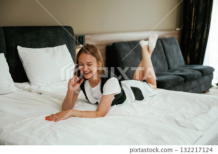 Lying down on the bed and using phone. Young chambermaid is in hotel room Lying down on the bed and using phone. Young chambermaid is in hotel room 132217124