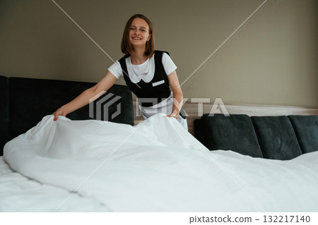 Large new pillow case on the bed. Young chambermaid is in hotel room 132217140