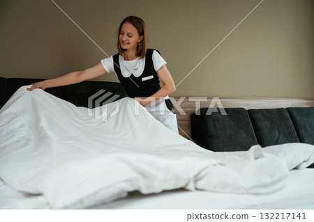 Large new pillow case on the bed. Young chambermaid is in hotel room 132217141