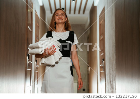 Holding fresh cloth for bed. Chambermaid is standing in the hotel corridor 132217150