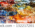 Close-up view of thick oil paint layers in blue, purple and orange tones on a messy palette. Captures abstract texture and creative energy of the painting process in a professional art studio. 132217201