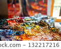 Close-up of a messy painter palette with thick dabs of oil paint in various bright colors. In the background, a blurry painting is visible, evoking creativity and inspiration. 132217216