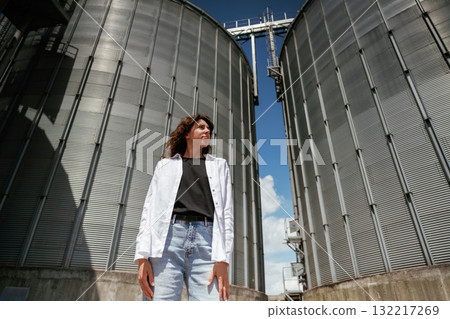 Confident worker standing in front of industrial silos under clear blue sky Confident worker standing in front of industrial silos under clear blue sky 132217269