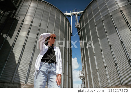 Looking far away. Confident worker standing in front of industrial silos under clear blue sky Looking far away. Confident worker standing in front of industrial silos under clear blue sky 132217270