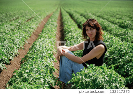Young woman sitting in lush green field of crops on sunny day 132217275