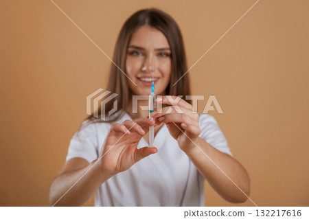 Syringe is in nurse hands. Young pretty woman is against background in the studio Syringe is in nurse hands. Young pretty woman is against background in the studio 132217616