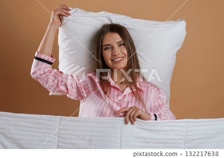 Front view, in pink pajama, waking up. Young pretty woman is against background in the studio Front view, in pink pajama, waking up. Young pretty woman is against background in the studio 132217638