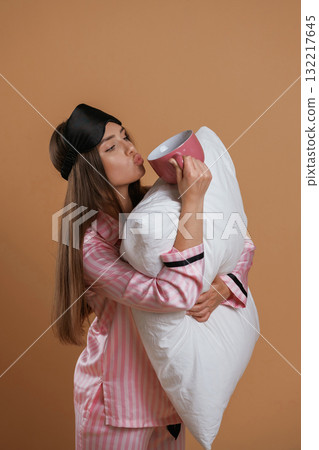 Conception of sleep products. With cup and pillow. Young pretty woman is against background in the studio Conception of sleep products. With cup and pillow. Young pretty woman is against background in the studio 132217645