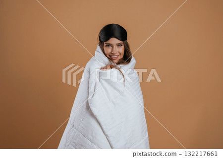 Wrapped in a blanket. Young pretty woman is against background in the studio Wrapped in a blanket. Young pretty woman is against background in the studio 132217661
