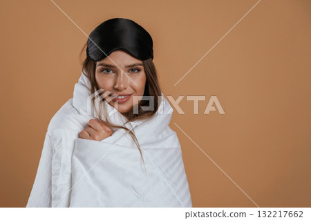 Wrapped in a blanket. Young pretty woman is against background in the studio 132217662