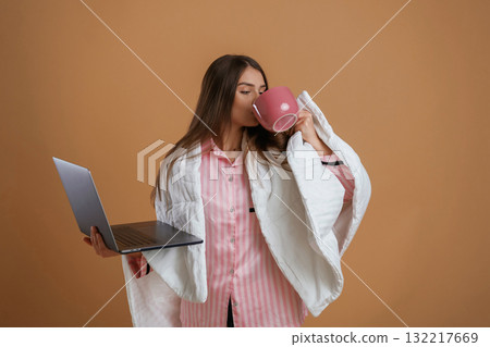 Holding laptop, in sleep clothes. Young pretty woman is against background in the studio 132217669