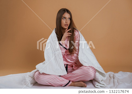 Sitting on the ground, in pajama, morning. Young pretty woman is against background in the studio Sitting on the ground, in pajama, morning. Young pretty woman is against background in the studio 132217674
