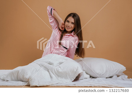 Doing morning stretches, on the ground. Young pretty woman is against background in the studio 132217680