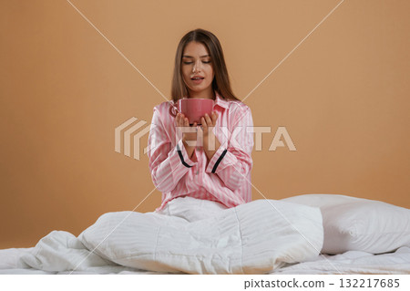 Drinking morning tea, holding cup. Young pretty woman is against background in the studio Drinking morning tea, holding cup. Young pretty woman is against background in the studio 132217685