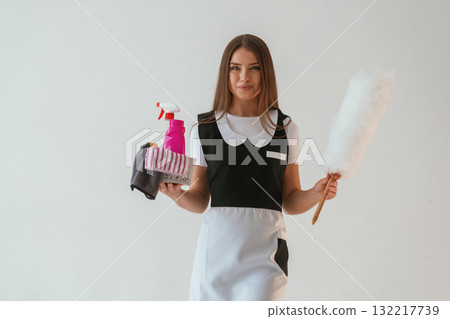 Chambermaid is with cleaning product and tool. Young pretty woman is against background in the studio 132217739