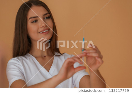 Vaccination concept, nurse is with syringe. Young pretty woman is against background in the studio 132217759