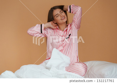 Morning time, in the bed. Young pretty woman is against background in the studio 132217761