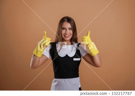 Brown backdrop, chambermaid is standing. Young pretty woman is against background in the studio 132217787