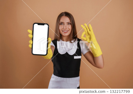 White copy space on smartphone, chambermaid is holding it. Young pretty woman is against background in the studio 132217799