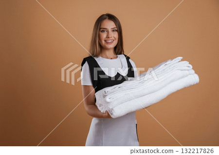 Fresh and clean towels in hands of chambermaid. Young pretty woman is against background in the studio 132217826