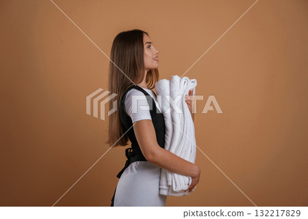 View from the side, chambermaid is with new towels. Young pretty woman is against background in the studio 132217829