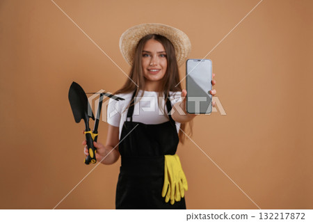 Modern technology, smartphone with copy space, gardener. Young pretty woman is against background in the studio Modern technology, smartphone with copy space, gardener. Young pretty woman is against background in the studio 132217872