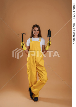 Equipment for gardening, in yellow clothes. Young pretty woman is against background in the studio Equipment for gardening, in yellow clothes. Young pretty woman is against background in the studio 132217880