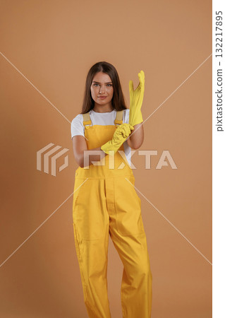 Professional wear, in yellow gloves. Young pretty woman is against background in the studio Professional wear, in yellow gloves. Young pretty woman is against background in the studio 132217895