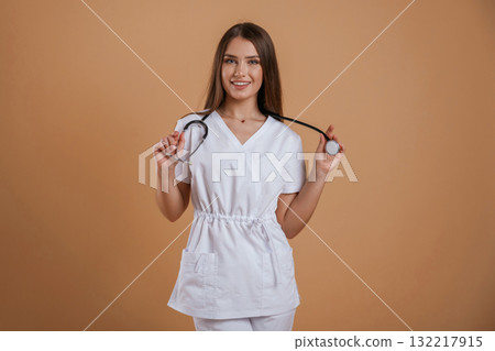 Standing with stethoscope. Young pretty woman is against background in the studio Standing with stethoscope. Young pretty woman is against background in the studio 132217915
