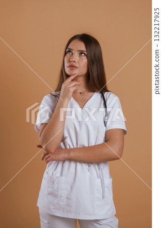 In doctor coat, with stethoscope. Young pretty woman is against background in the studio In doctor coat, with stethoscope. Young pretty woman is against background in the studio 132217925