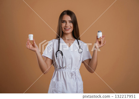 Pills in hands of doctor or a nurse. Young pretty woman is against background in the studio Pills in hands of doctor or a nurse. Young pretty woman is against background in the studio 132217951