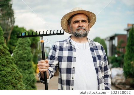 Standing with tools. Senior gardener is at work at daytime Standing with tools. Senior gardener is at work at daytime 132218092